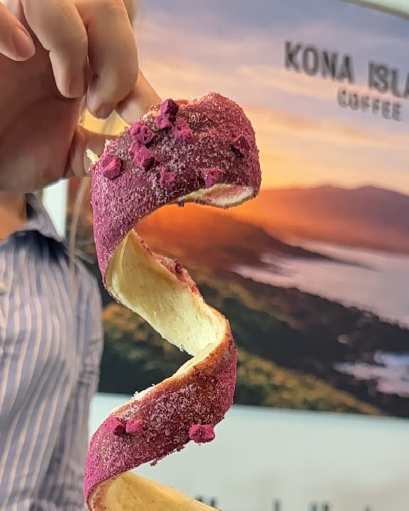 A dragonfruit chimney cake, its stretched spiral lifted from the cup, Kona Island Coffee branding visible.